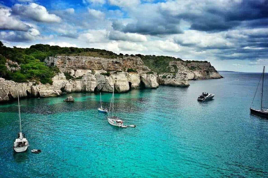 Sailboats in  the water and along the rugged coast of Menorca Spain.